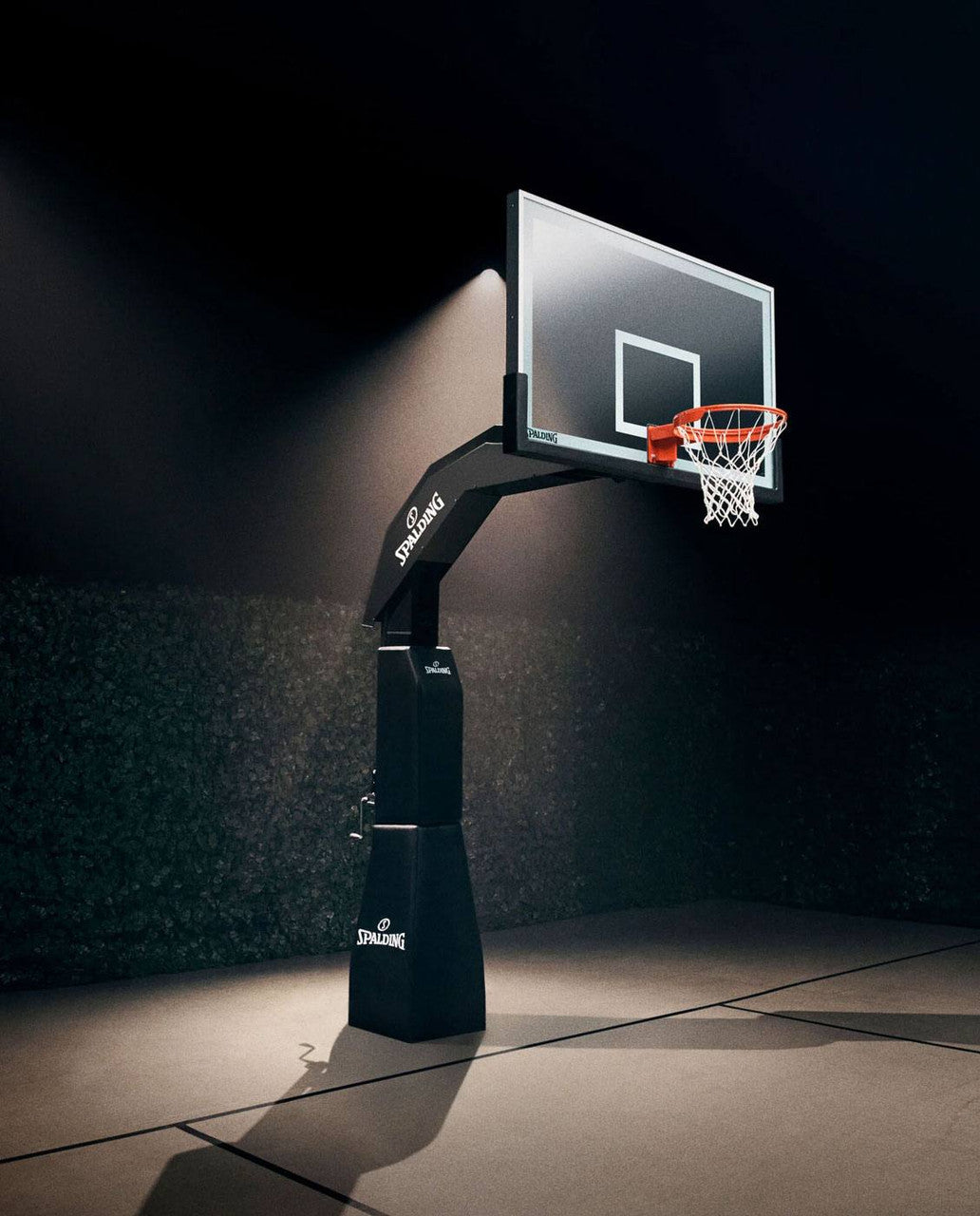Spalding arena renegade in-ground basketball hoop set in a dimly lit basketball court.