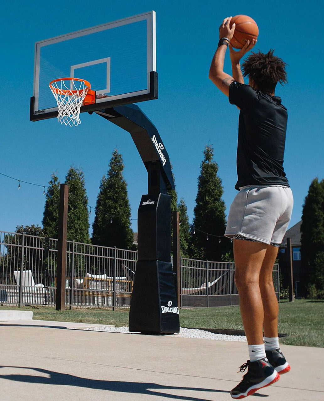 Player shooting a basketball at a Spalding Arena Renegade In-Ground Basketball Hoop in a backyard setting.